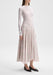 A person wearing a sheer white long-sleeve top layered over a camisole, paired with a mid-length, flowy pink skirt with a delicate floral pattern and black pointed-toe flats.