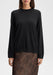 Front-facing mid-length view of a model standing upright with arms relaxed at her sides, wearing a black long-sleeve knit sweater paired with a sheer brown floral lace skirt against a plain background.