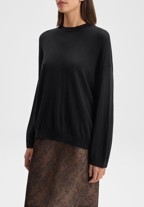 The model is shown in a slight three-quarter front view, angled gently to the left. Her shoulders are relaxed, arms resting naturally by her sides, with her head subtly turned left, highlighting the front and drape of the sweater and the top of the skirt.