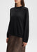 The model is shown in a slight three-quarter front view, angled gently to the left. Her shoulders are relaxed, arms resting naturally by her sides, with her head subtly turned left, highlighting the front and drape of the sweater and the top of the skirt.