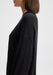 The model is shown in a side profile, facing left. Only the upper torso is visible, with her shoulders relaxed and arms down by her sides, highlighting the fit and drape of the sweater from the side.