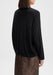 The model is shown from the back in a three-quarter view, with her body angled slightly to the right. Her head is gently turned to the side, and her arms rest naturally by her sides, highlighting the back and drape of the black sweater and the top of the lace skirt.