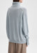 Back-facing view of the model standing upright with her body slightly angled to the side, arms relaxed at her sides, showcasing the rear of a light blue oversized turtleneck sweater paired with beige trousers.