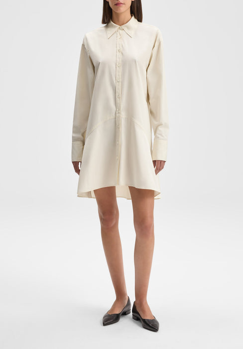 The model is standing upright in a relaxed posture, facing away from the camera with her back visible. Her body is slightly angled to one side, with arms resting naturally at her sides and one leg subtly positioned behind the other, giving a gentle, poised stance.