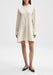 The model is standing upright in a relaxed posture, facing away from the camera with her back visible. Her body is slightly angled to one side, with arms resting naturally at her sides and one leg subtly positioned behind the other, giving a gentle, poised stance.