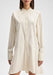 Front-facing view of a model standing upright with arms relaxed at her sides, wearing a cream long-sleeve button-down shirt dress with a pointed collar and softly flared hem against a plain background.