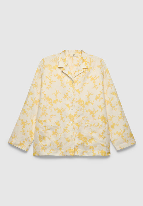 A cream-colored long-sleeve shirt with a relaxed fit, featuring a notched collar, front button closure, patch pockets, and a delicate yellow floral print, displayed against a plain background.
