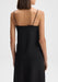 Back view close-up of a model from shoulders to hips wearing a black sleeveless top with thin spaghetti straps, standing upright with arms relaxed at her sides against a plain background.