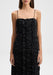 Front-facing view of the model standing upright with shoulders squared and arms relaxed straight at her sides, wearing a black spaghetti-strap dress with vertical ruffle detailing down the front.