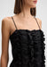 Close-up three-quarter view of the model’s upper body, slightly angled to the side with shoulders turned and head subtly facing forward, wearing a black spaghetti-strap dress with ruffled detailing across the bodice.