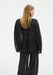 Back view of a model wearing a sheer black long-sleeve blouse with gathered shoulders and matching translucent trousers, highlighting the lightweight fabric and relaxed silhouette.