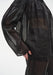 Close-up side view of a sheer black long-sleeve blouse with gathered shoulder detailing, showing the lightweight, semi-transparent fabric layered over matching trousers and revealing the silhouette beneath.