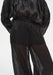 Close-up of a sheer black outfit showing a loose blouse tucked into lightweight, semi-transparent trousers with a soft elastic waistband, revealing the silhouette of the legs beneath and emphasizing the airy, textured fabric.