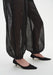 Close-up of sheer black billowy trousers with elasticated cuffs at the ankles, revealing the legs beneath, paired with black pointed low-heel shoes.