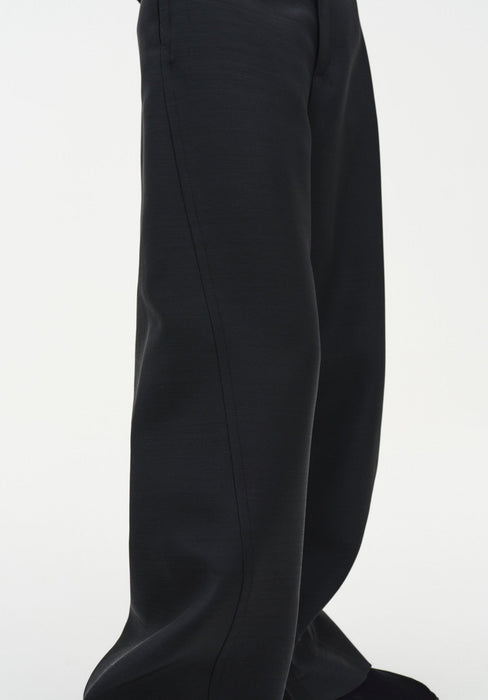 Close-up of black wide-leg trousers highlighting the smooth fabric and a vertical seam running down the leg, showing a clean, structured drape.