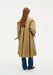 Back view of a model wearing a beige trench-style coat with a flared silhouette and cuff straps, paired with wide-leg blue jeans and black pointed shoes.