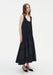 Side view of a model wearing a sleeveless black midi dress with a scoop neckline and a softly flared, semi-sheer panelled skirt, paired with black pointed shoes.