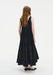 Back view of a model wearing a sleeveless black midi dress with a scoop back and a softly flared, semi-sheer panelled skirt, paired with black pointed shoes.