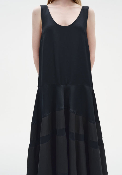 Close-up of a sleeveless black dress featuring a scoop neckline and a softly gathered, semi-sheer panelled skirt with subtle texture.