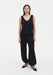 Front view of a woman wearing a black sleeveless scoop-neck tank top with a relaxed fit, paired with loose, draped black trousers gathered at the ankles and black pointed heels.