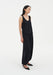 Three-quarter side view of a woman wearing a black sleeveless scoop-neck tank top with a relaxed silhouette, paired with loose, fluid black trousers gathered at the ankles and black pointed heels.