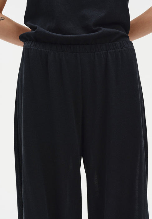 Close-up of black trousers featuring a soft elasticated waistband and fluid, draped fabric with a relaxed fit.