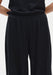 Close-up of black trousers featuring a soft elasticated waistband and fluid, draped fabric with a relaxed fit.