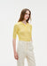 Three-quarter view of a model wearing a fitted yellow ribbed short-sleeve polo top with buttons, paired with high-waisted cream trousers.