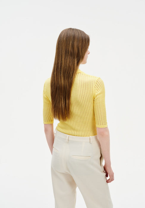 Back view of a model wearing a fitted yellow ribbed short-sleeve top tucked into high-waisted cream trousers with welt back pockets.