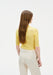 Back view of a model wearing a fitted yellow ribbed short-sleeve top tucked into high-waisted cream trousers with welt back pockets.