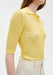 Close-up of a fitted yellow ribbed knit polo top with short sleeves and button placket, tucked into high-waisted cream trousers.