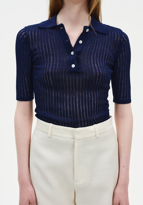 A close-up front view of a woman’s torso, showing a relaxed upright posture with her arms at her sides against a plain background.