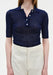 A close-up front view of a woman’s torso, showing a relaxed upright posture with her arms at her sides against a plain background.