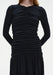 Close-up of a black long-sleeve dress showing ruched detailing along the front bodice, with gathered fabric creating a textured, fitted silhouette above a softly gathered skirt.