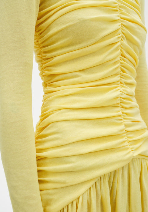A close-up detail of a woman’s torso highlighting ruched fabric and gathered seams, with soft folds creating texture and movement against a plain background.