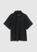A black short‑sleeved top laid flat on a light gray background, featuring a built‑in scarf detail draped around the neckline.