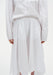 Close-up of a white outfit showing a long-sleeve top tucked into a high-waisted skirt with soft pleats and a fluid, asymmetrical hem.