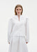 Front view of a model wearing a white blouse with a V-slit neckline and structured shoulders, paired with a matching flowing skirt, shown against a plain background.