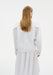 Back view of a model wearing a white blouse with structured shoulders and long sleeves, paired with a flowing white skirt, shown against a plain background.