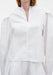 Close-up of a white blouse with a clean V-slit neckline, structured shoulders, and long sleeves in a smooth, crisp fabric.