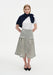 A woman stands facing forward with a slight three-quarter angle against a plain white background, wearing a white short-sleeve top with a navy sweater draped over her shoulders, paired with a light gray textured midi skirt with flap pockets and a front slit, and black pointed heels.