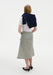 Rear three-quarter view of a woman against a plain white background, wearing a white short-sleeve top with a navy sweater draped over her shoulders, paired with a light gray textured midi skirt and black pointed heels.