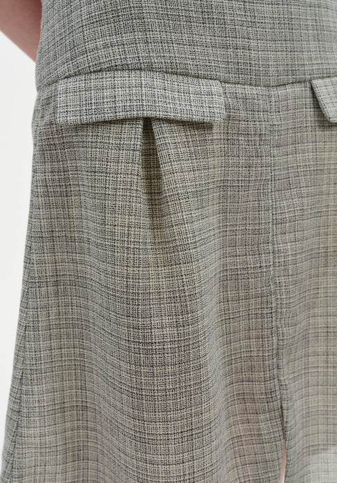 Close-up of a textured, light gray woven skirt featuring a subtle check pattern, with a structured waistband and a flap pocket detail at the hip.