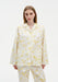 Front view of a woman wearing a white button-up shirt and matching trousers with a soft yellow floral pattern, featuring a relaxed fit with a notched collar and patch pockets, set against a plain studio background.