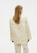 Back view of a woman wearing a white long-sleeve top and matching trousers with a soft yellow floral pattern, showing the relaxed fit and drape of the outfit against a plain studio background.