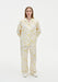 Front view of a model wearing a cream two-piece set with a yellow abstract floral print, featuring a long-sleeve collared button-up top with patch pockets and relaxed straight-leg trousers, paired with white shoes.