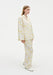 Side view of a model wearing a cream two-piece set with a yellow abstract floral print, featuring a long-sleeve collared jacket-style top and relaxed straight-leg trousers, paired with white shoes.