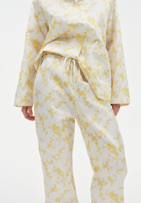 Close-up of cream trousers with a yellow abstract floral print, featuring a relaxed fit, drawstring waistband, and lightweight draped fabric, paired with a matching button-up top.