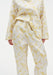 Close-up of cream trousers with a yellow abstract floral print, featuring a relaxed fit, drawstring waistband, and lightweight draped fabric, paired with a matching button-up top.