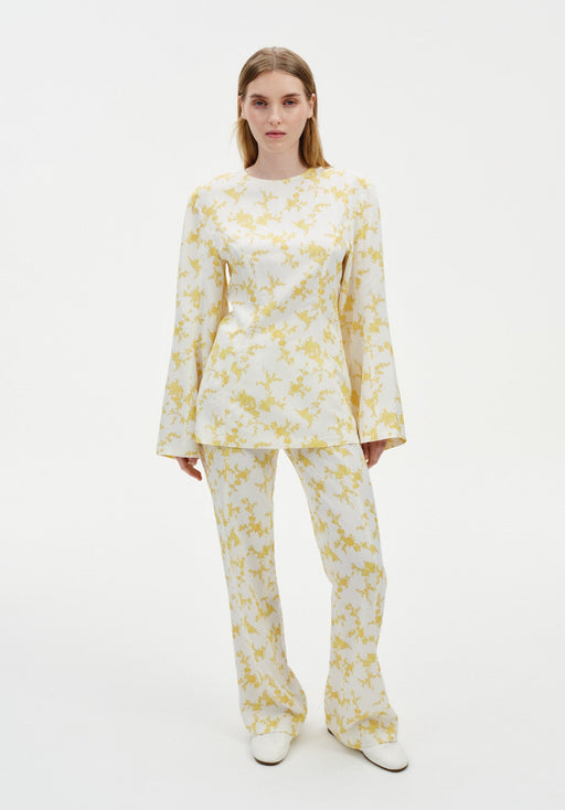 Model wearing a coordinated cream outfit with a yellow abstract floral print, featuring a long-sleeve tunic top with flared cuffs and matching straight-leg trousers, styled with white shoes.